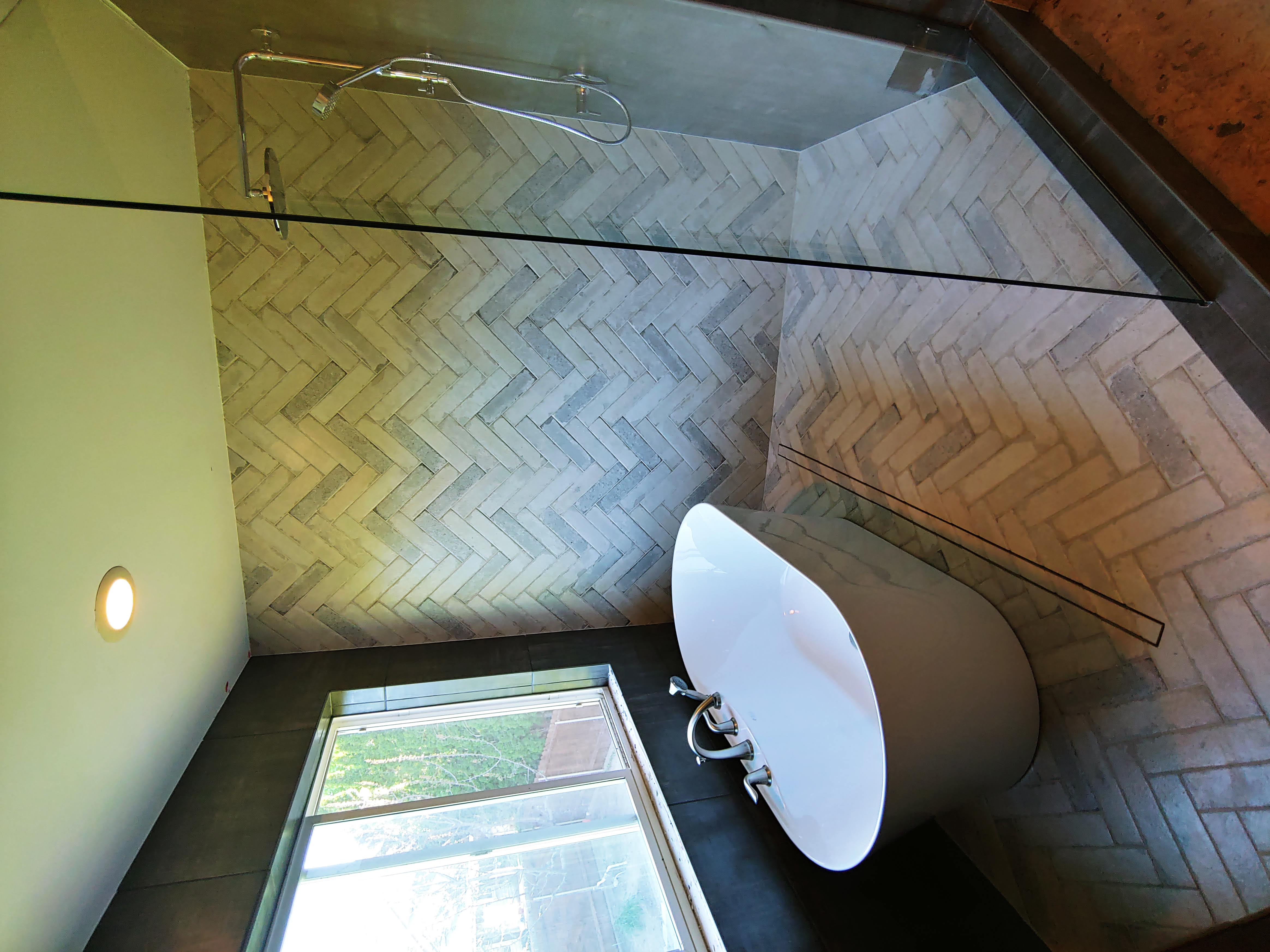 Modern bathroom with a white freestanding tub and glass walk-in shower with herringbone tile.