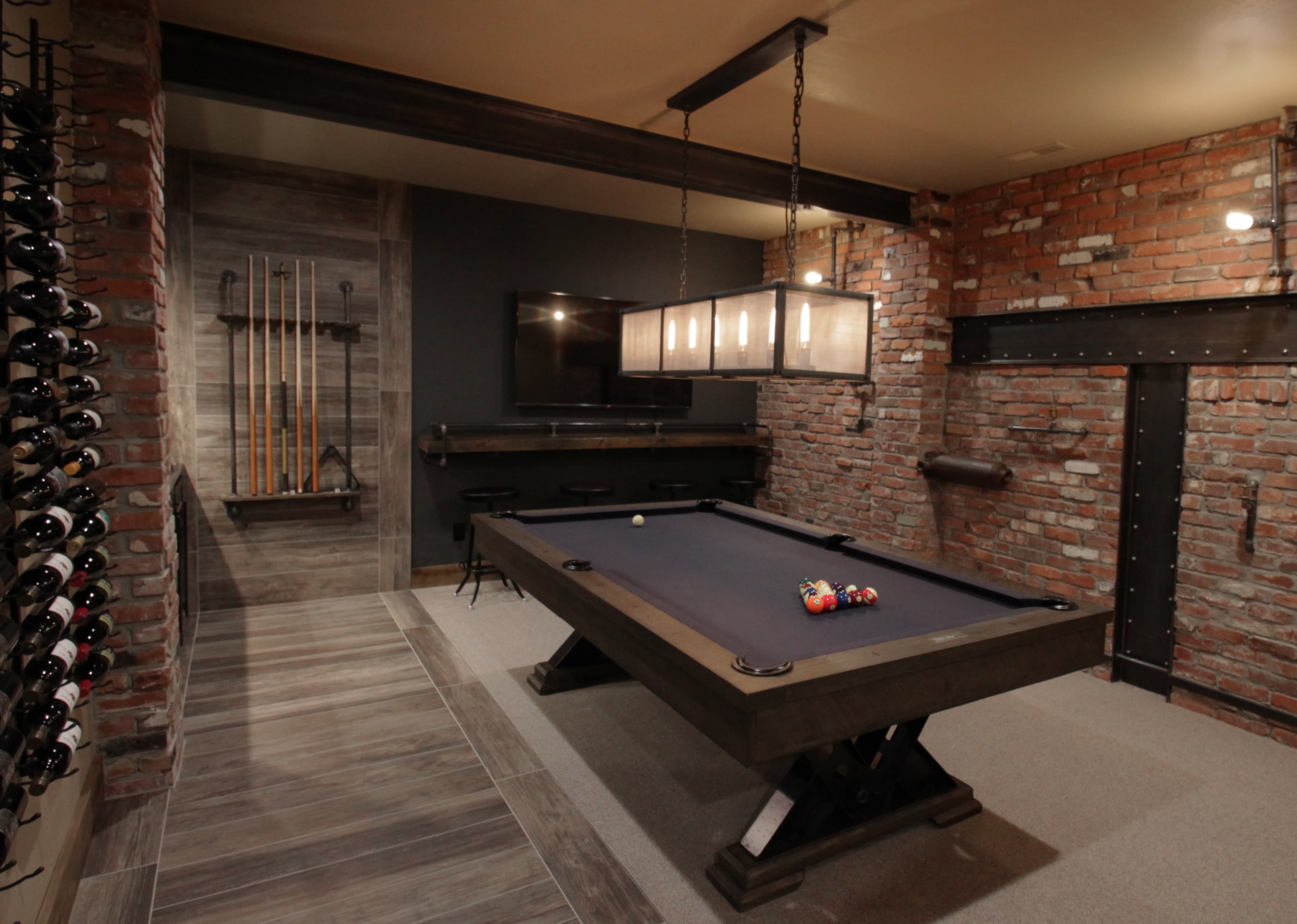 Modern industrial game room featuring a pool table, brick walls, wine rack, and hanging light.