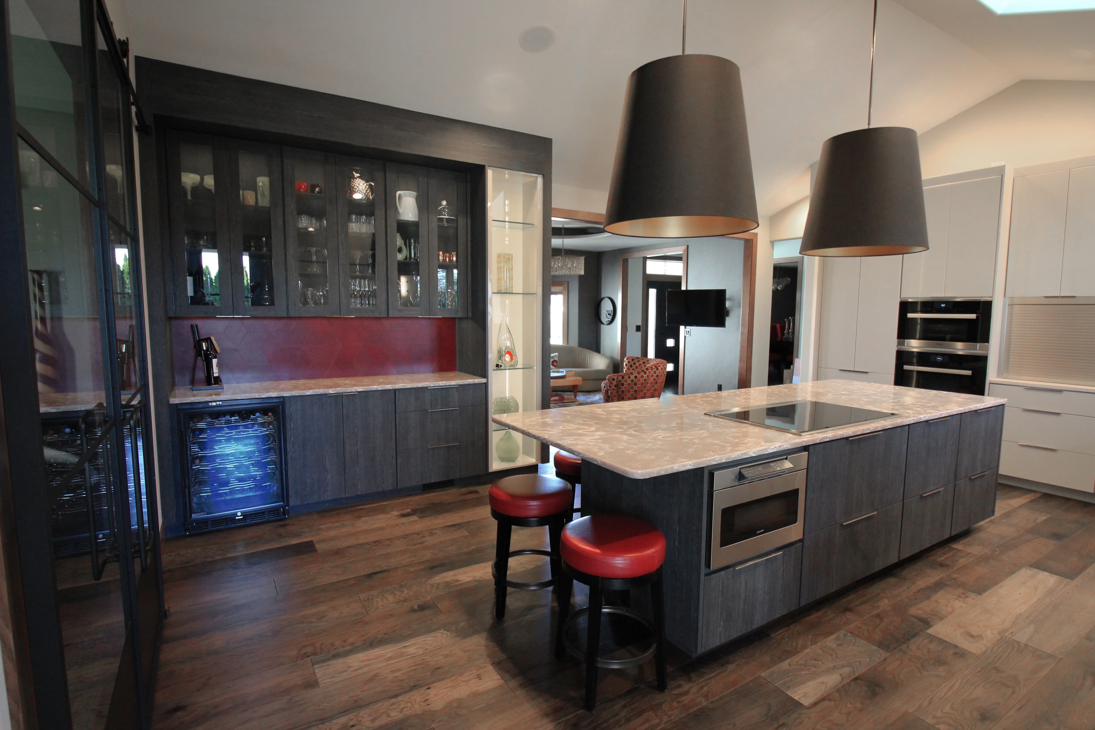 Modern kitchen featuring a large island, red bar stools, and oversized black pendant lights.