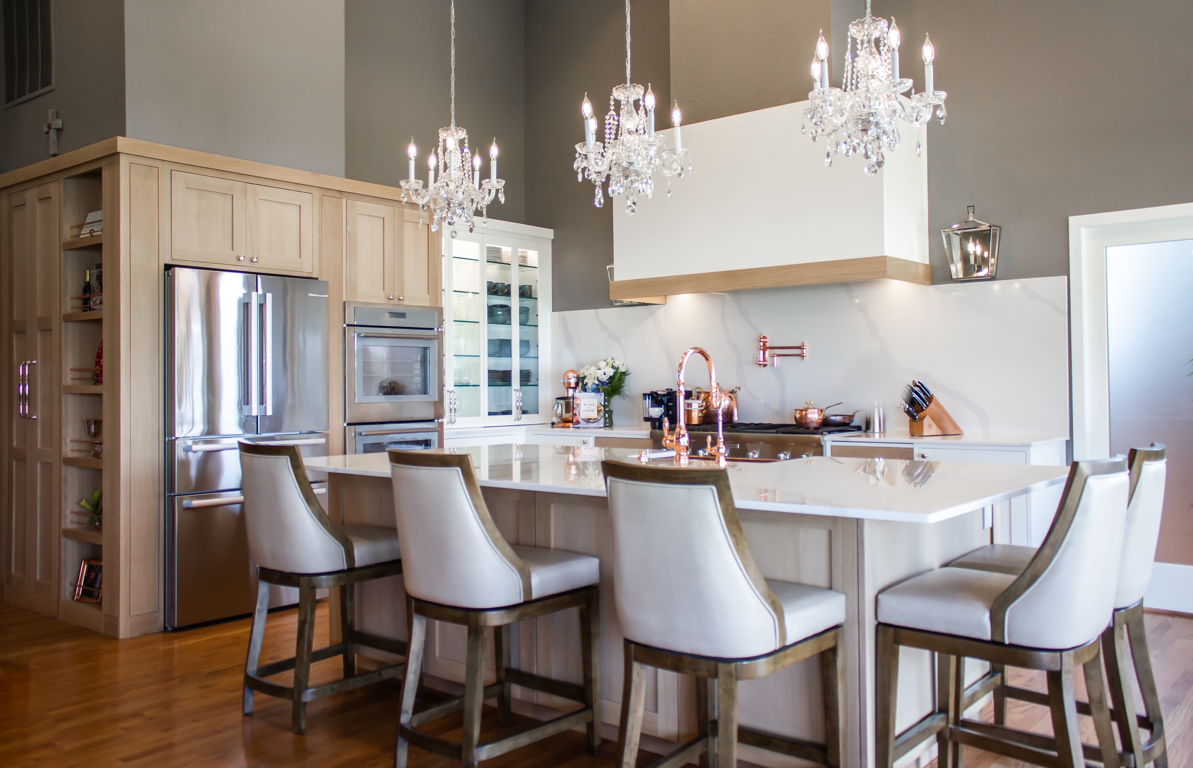 Modern kitchen with crystal chandeliers, light wood cabinets, and a marble island with bar stools.