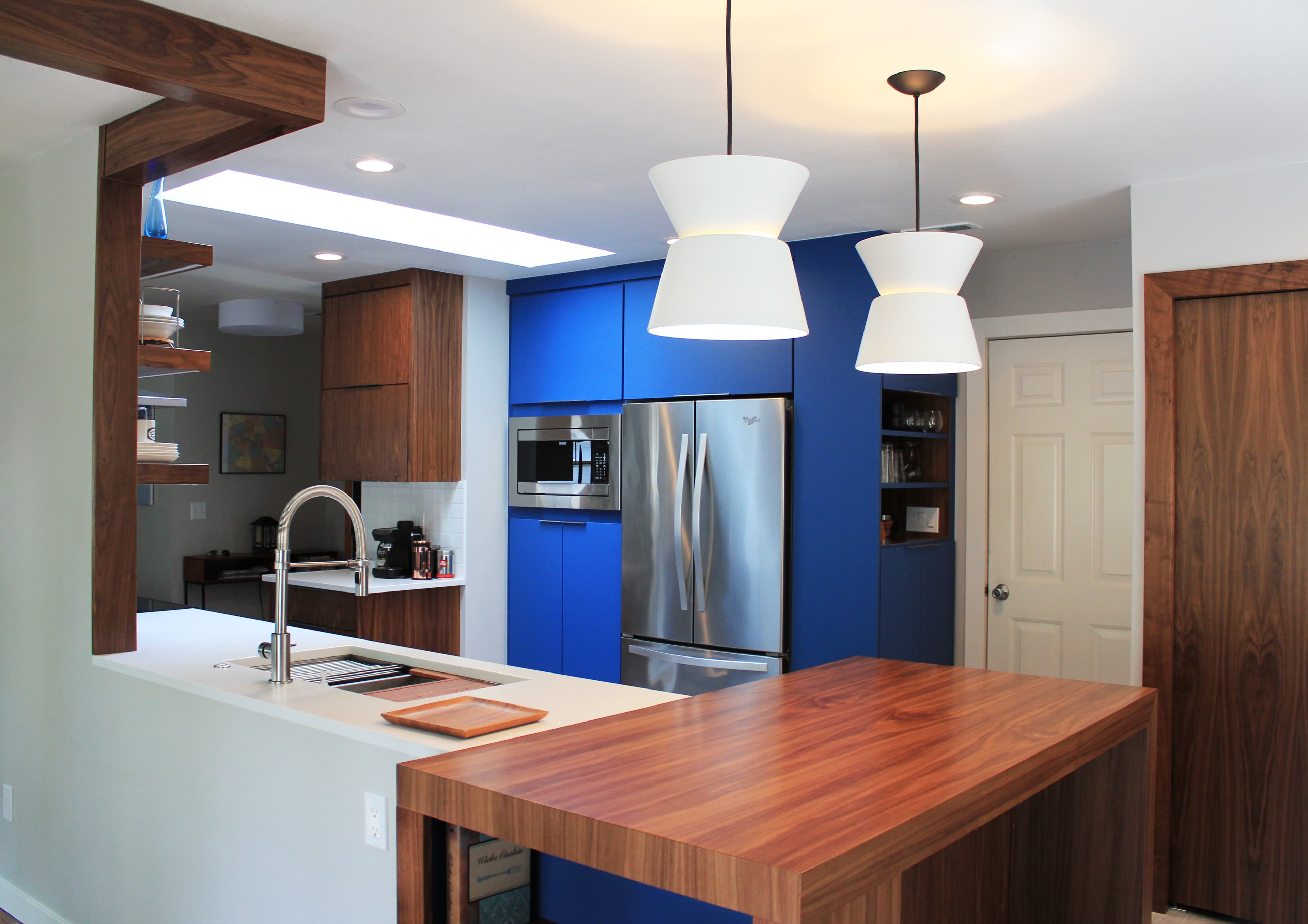 Modern kitchen with blue cabinetry, walnut wood island, white countertops, and hourglass pendant lights.