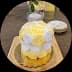 Small cake decorated with yellow and white frosting rosettes on a wooden board.