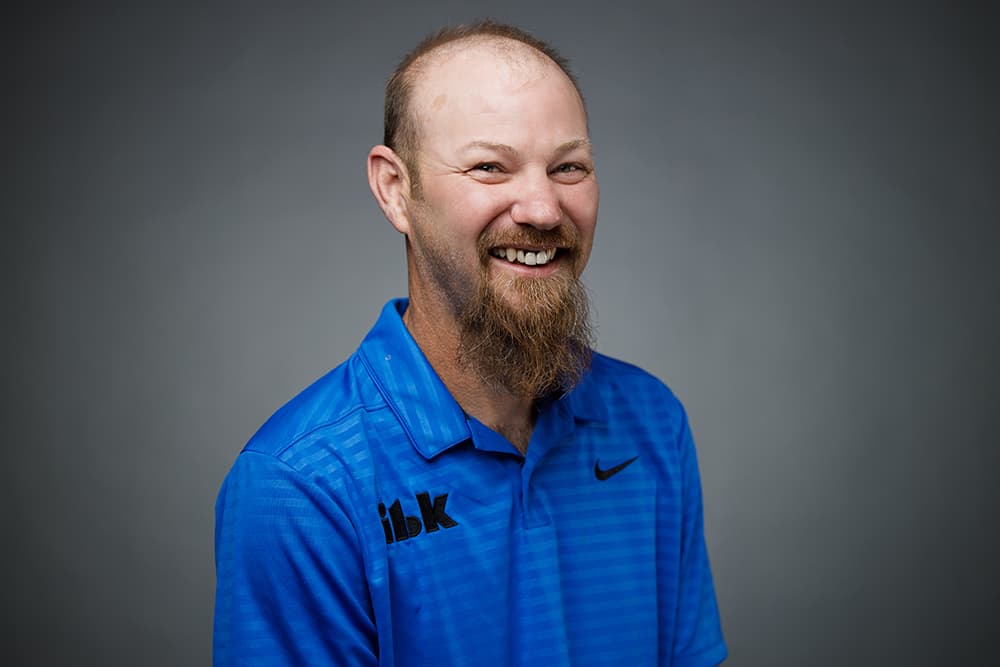 Smiling man with a brown beard and thinning hair wearing a blue Nike polo shirt.