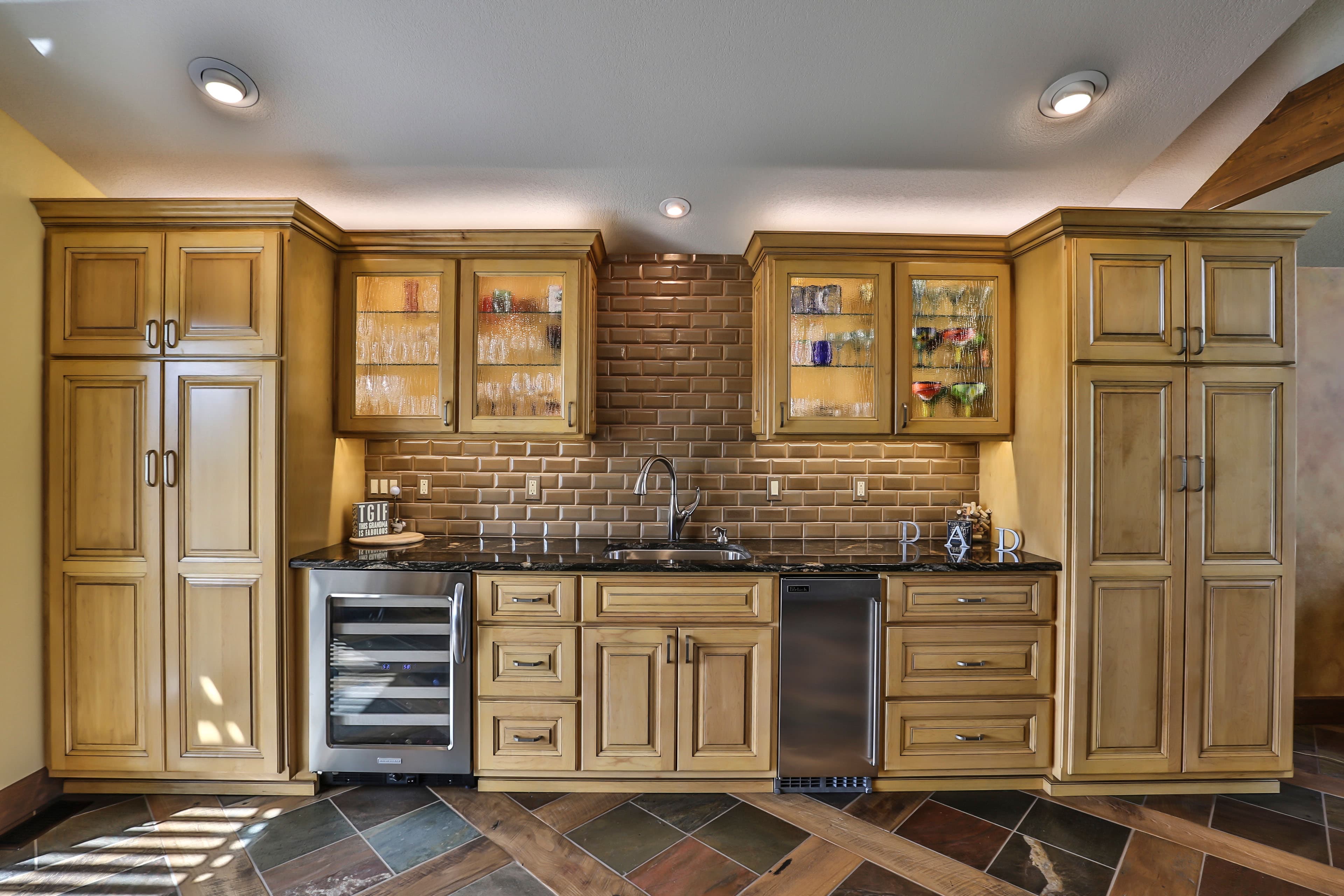 Light wood home bar featuring brown subway tile, granite countertops, and a built-in wine fridge.