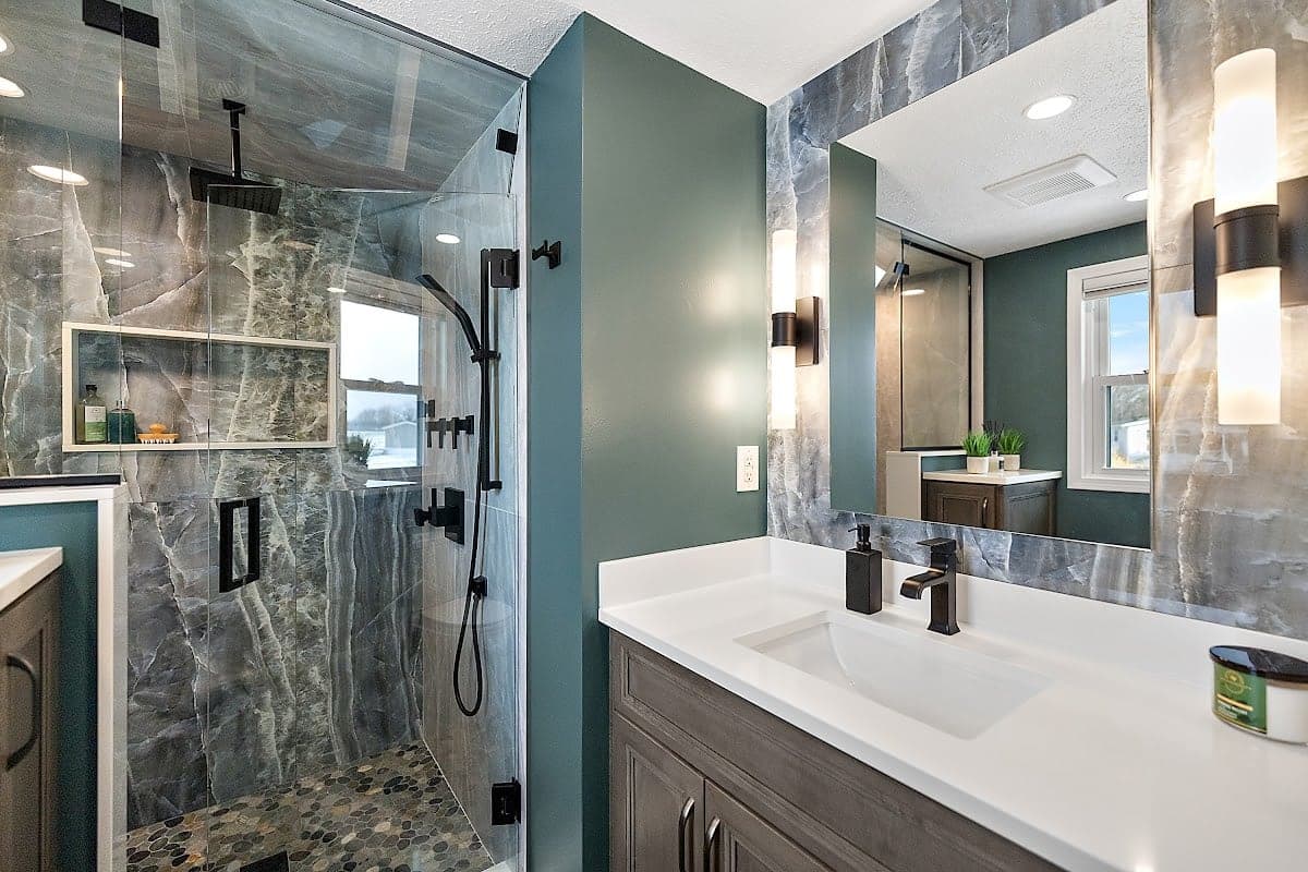 Modern bathroom with marble-tiled glass shower, teal walls, and white vanity with black fixtures.