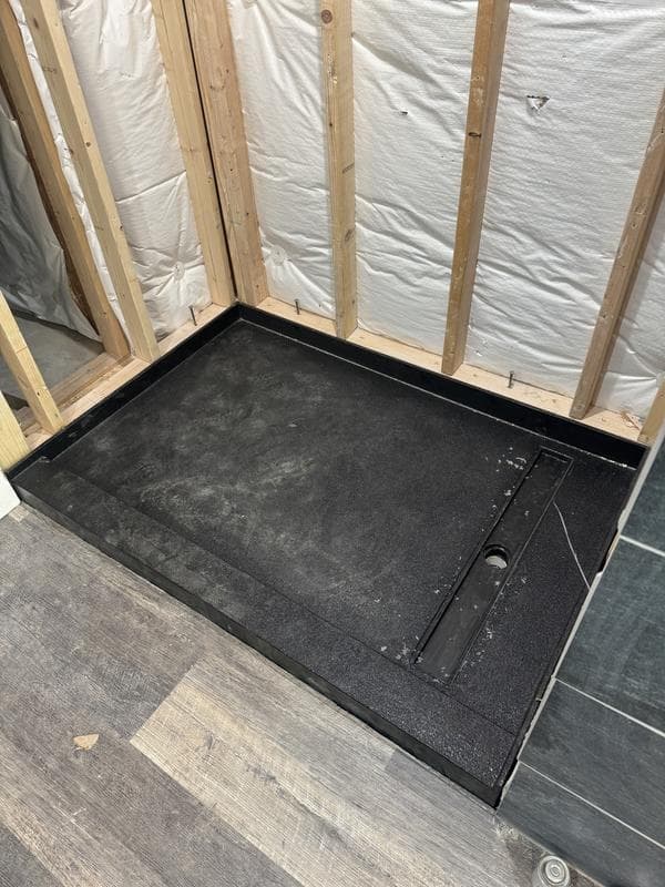 Black rectangular shower pan with a linear drain installed in a framed bathroom corner.